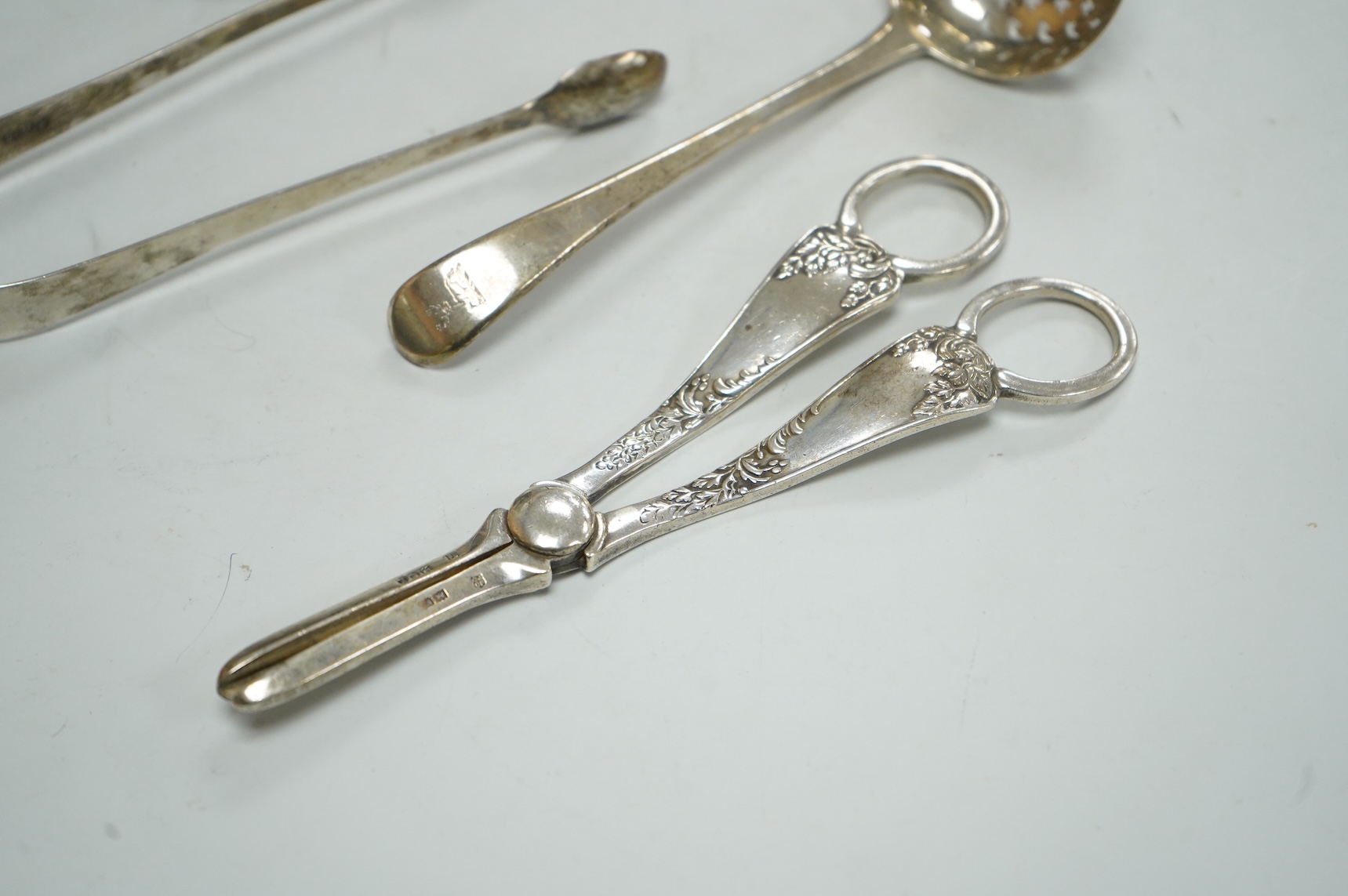 A pair of George V silver grape shears, Josiah Williams & Co, London, 1912, 16.2cm, together with a George III silver Old English pattern sifter spoon, Eley & Fearn, London, 1801, a similar pair of sugar tongs, London, 1